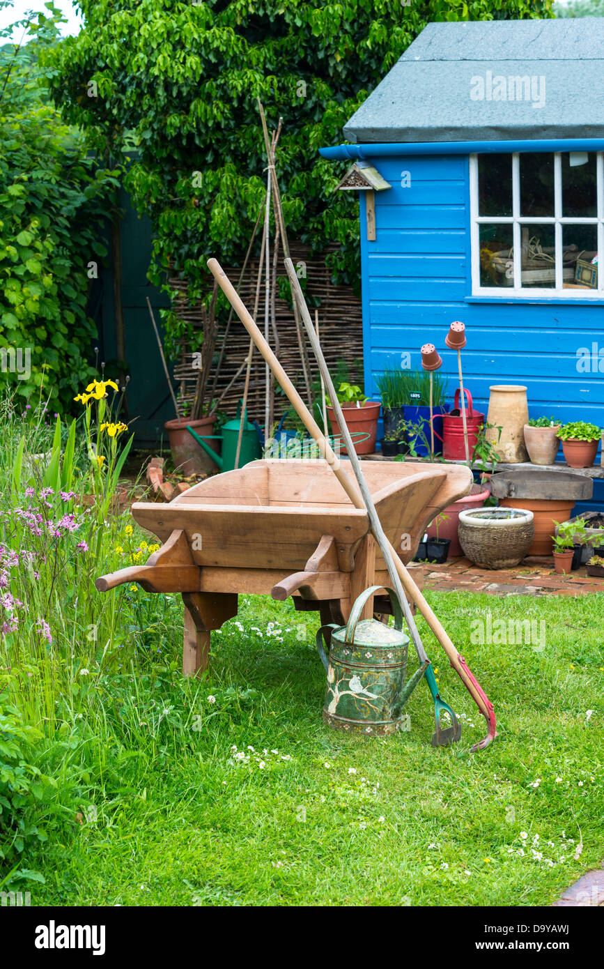 Country garden scene with wooden wheelbarrow, blue potting shed and wildlife area to the left, Norfolk, England, June Stock Photo