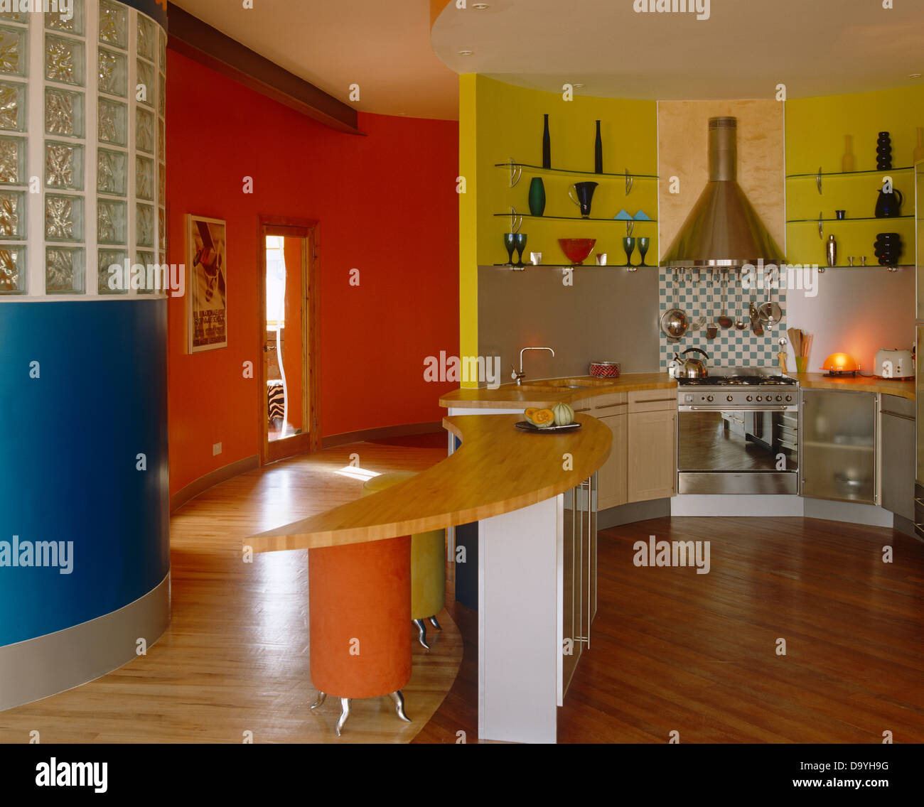 Curved breakfast bar and wooden flooring in vibrant open plan red and yellow kitchen with