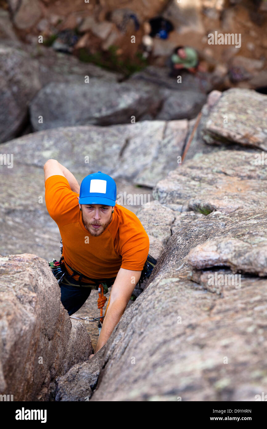 A male climber wearing an orange shirt, blue jeans, and a bright blue