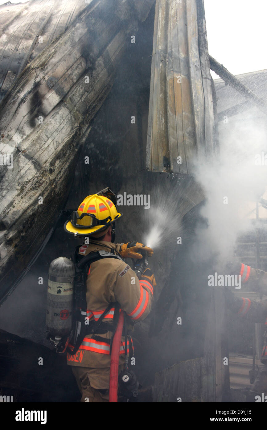 A firefighter spraying water on a structure fire hotspot Stock Photo ...