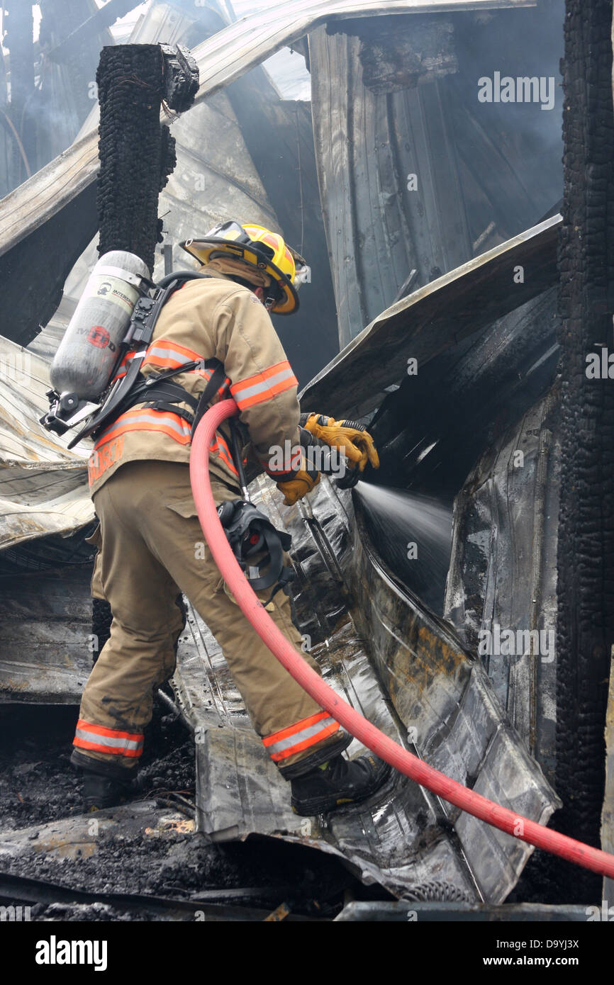 A firefighter pouring water on a structure fire hot spot Stock Photo
