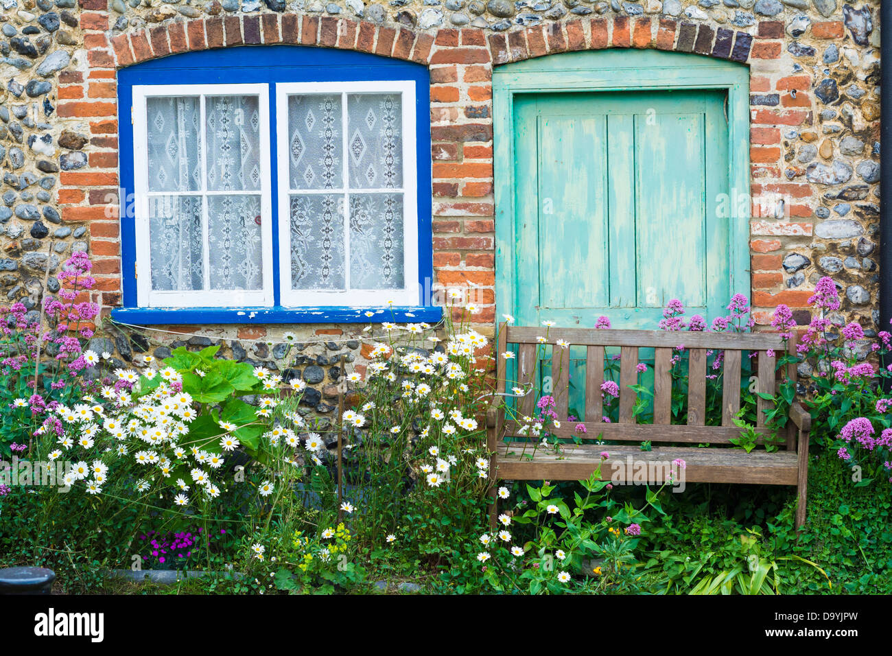 Flint faced cottage with summer flowers and wooden,garden bench, Norfolk, England, June Stock Photo
