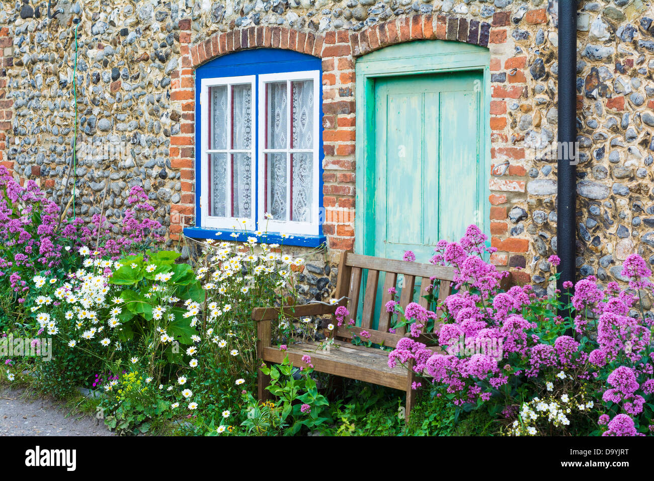 Flint faced cottage with summer flowers and wooden,garden bench, Norfolk, England, June Stock Photo