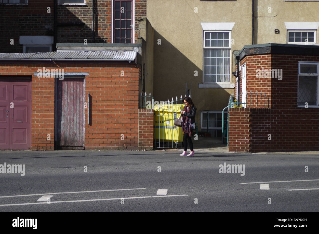 A young woman / young lady walking down the street using her mobile phone. Stock Photo