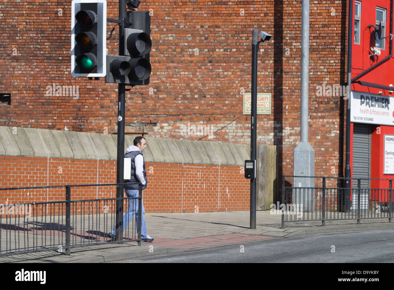 A man walking on the pavement next to a pelican crossing and a set of traffic lights. Stock Photo