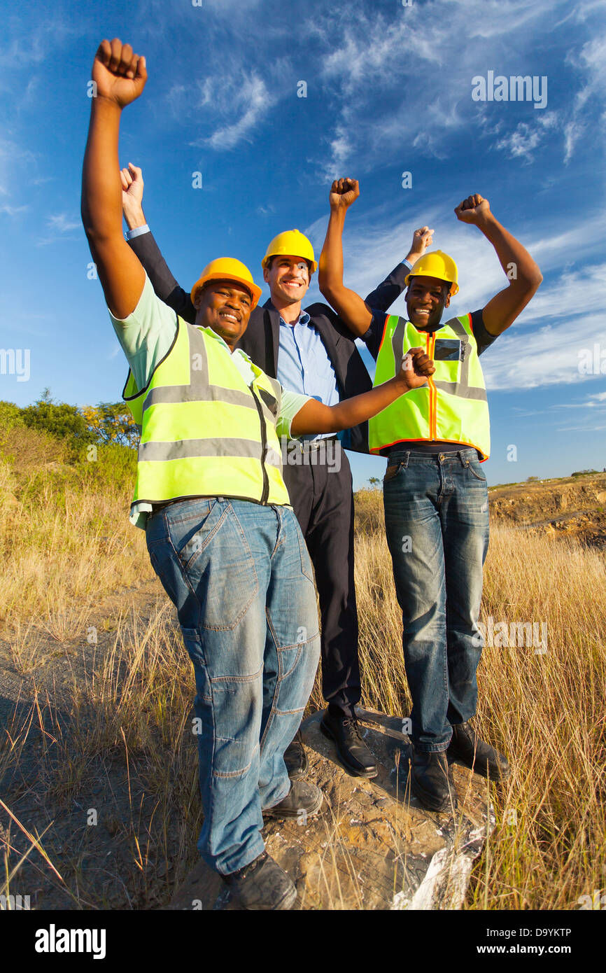 successful construction workers with arms outstretched outdoors Stock