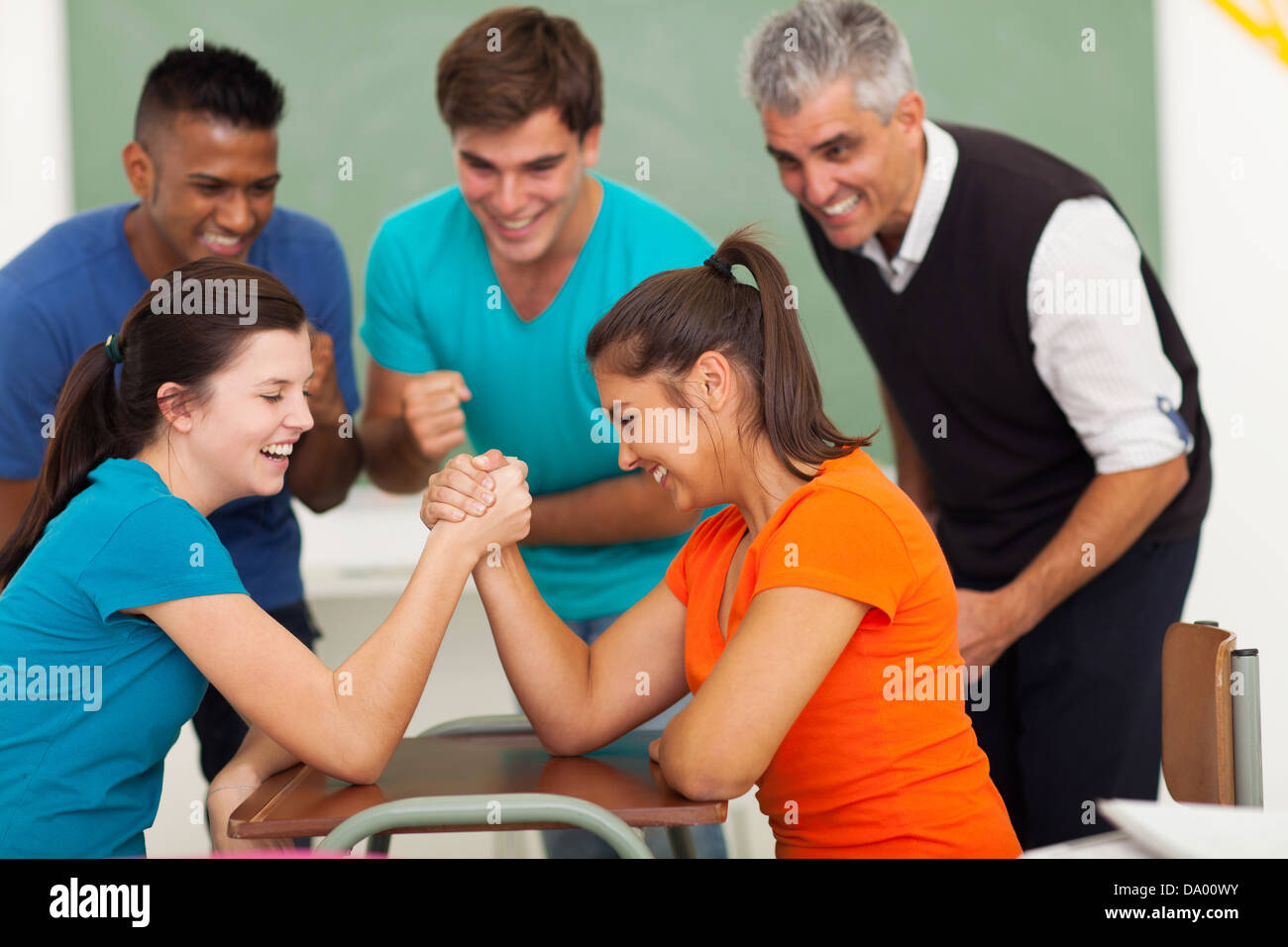cheerful female high school students playing arm wrestling in classroom