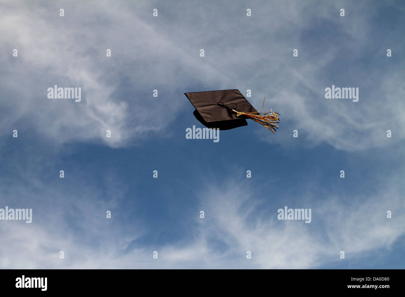 Graduation cap flying through the air at a graduation ceremony against a blue sky with white clouds, Successfully flying free! Stock Photo