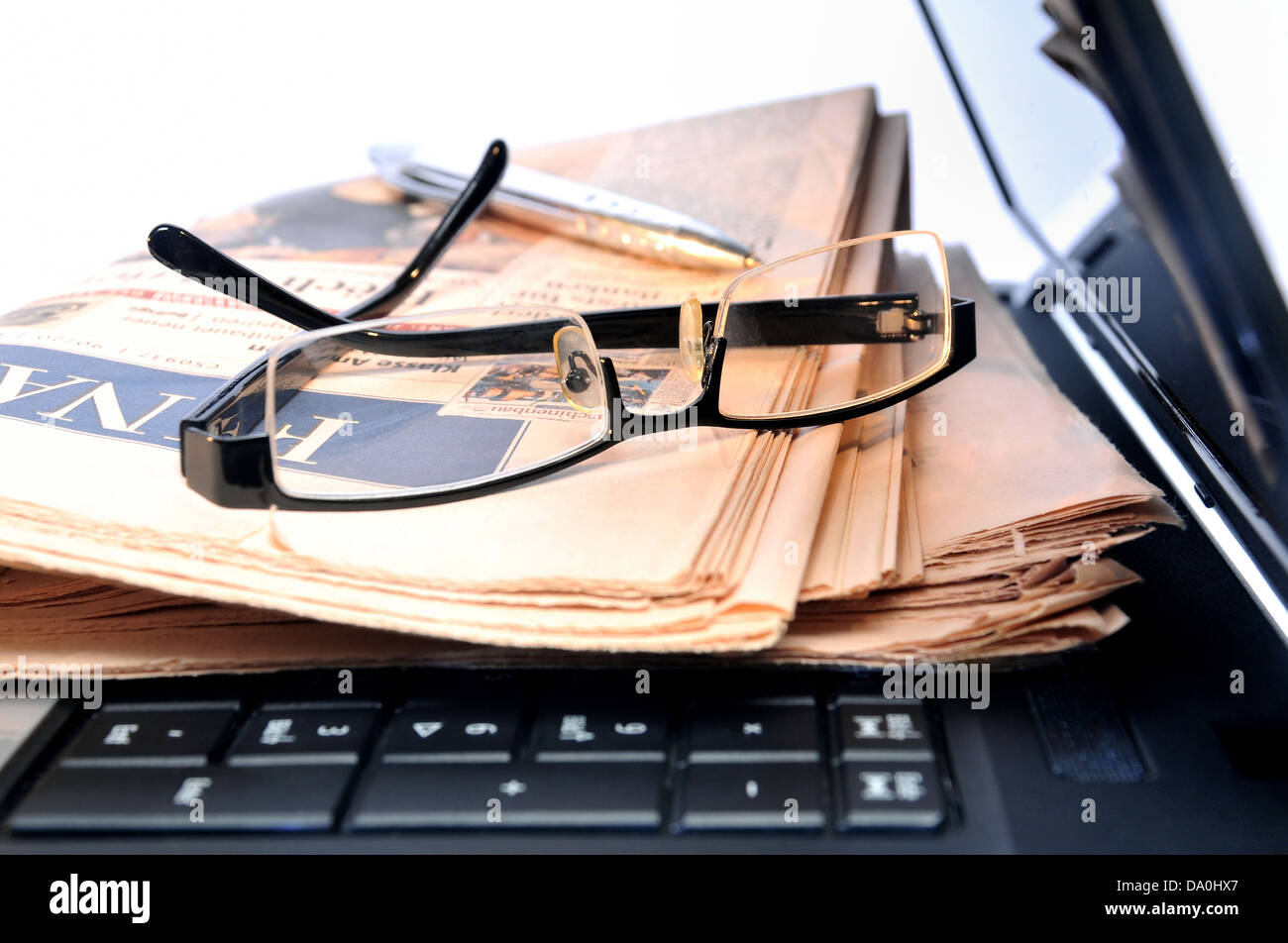 Newspaper, glasses and ball pen on top of a laptop Stock Photo