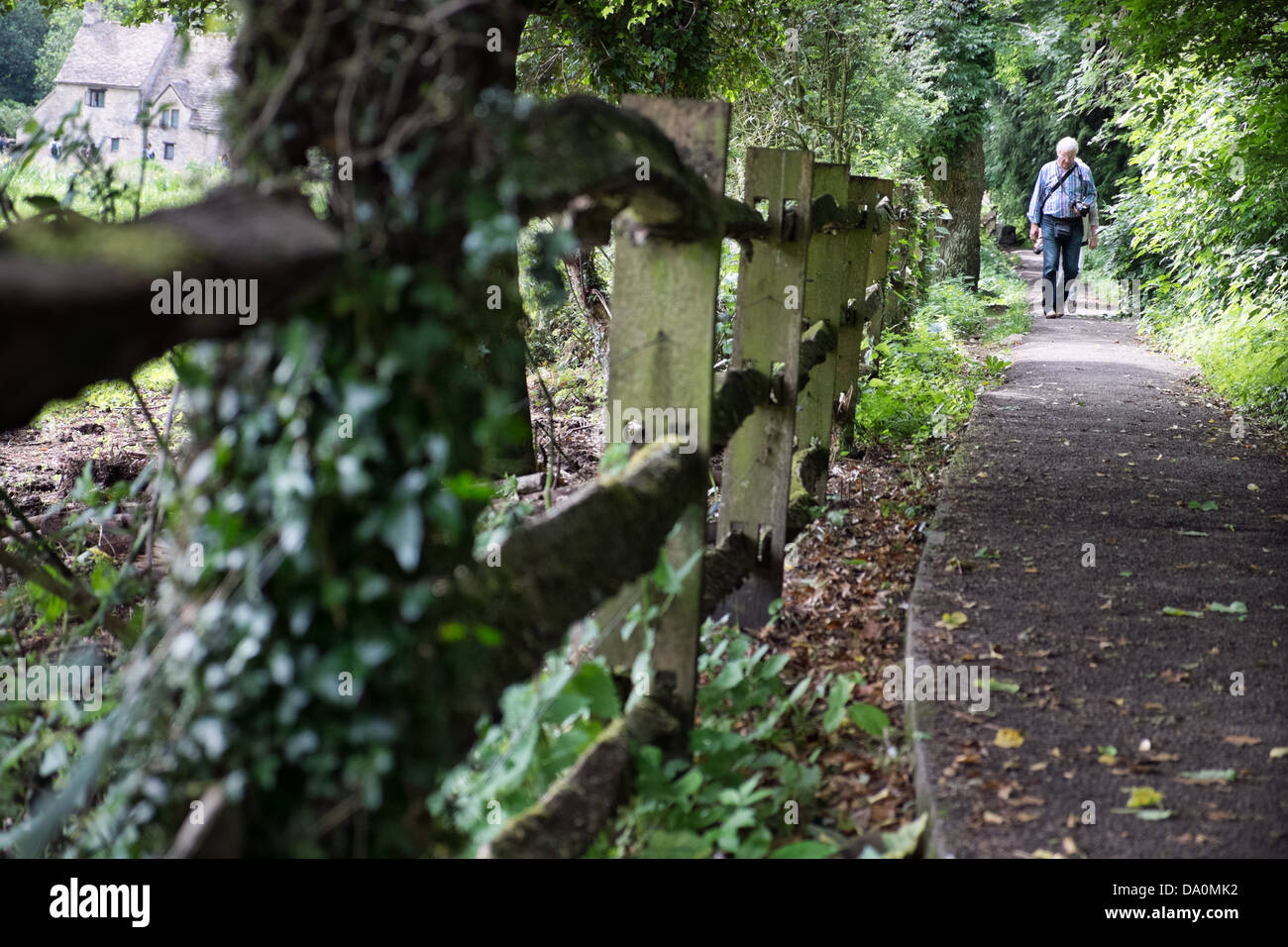 A tourist walking a path in Bibury, Gloucestershire, UK. With historic attraction, Arlington Row in the distance. Stock Photo