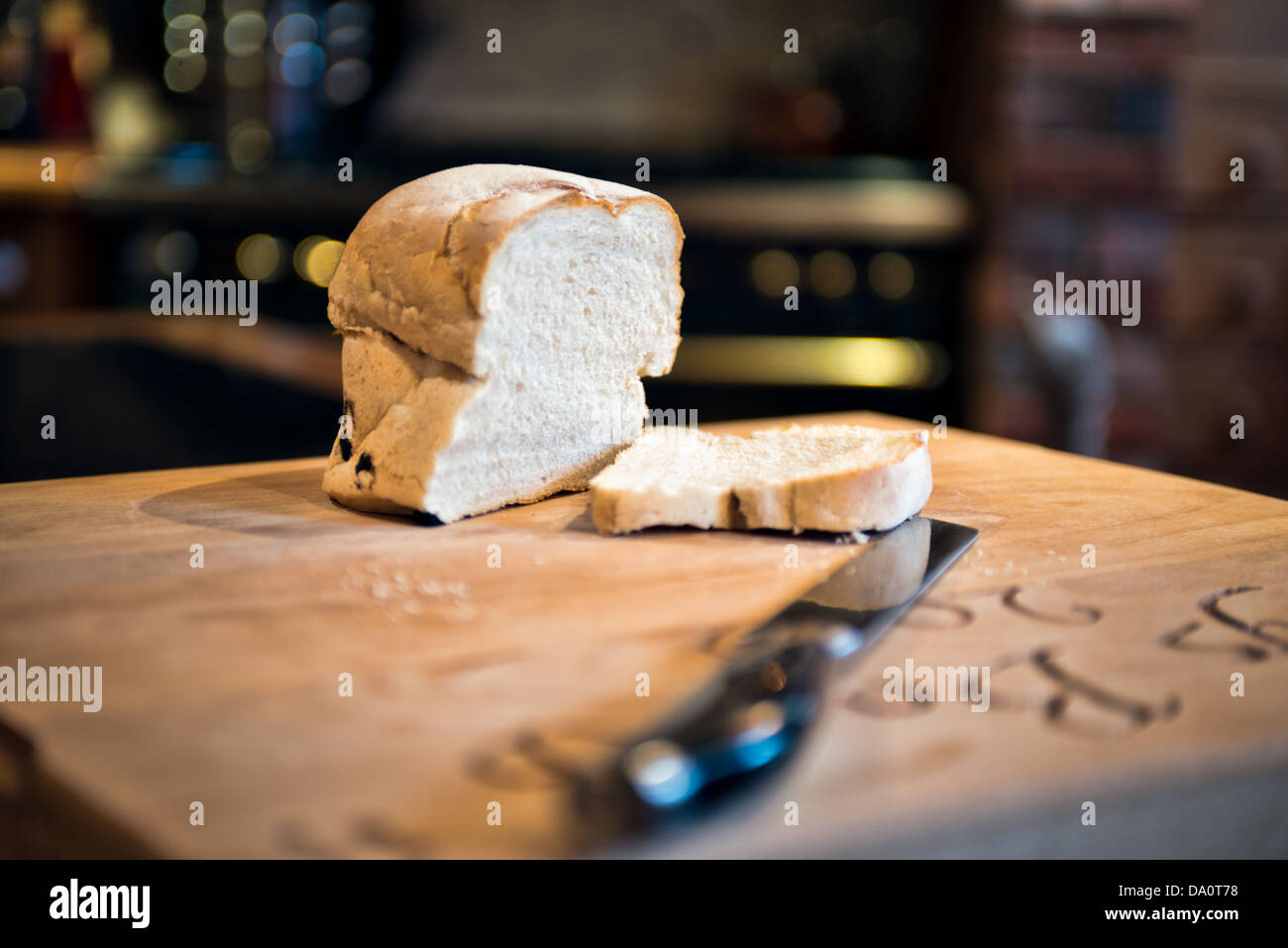 A Sliced loaf of white bread on a breadboard with a de-focused carving knife in a country Kitchen Stock Photo