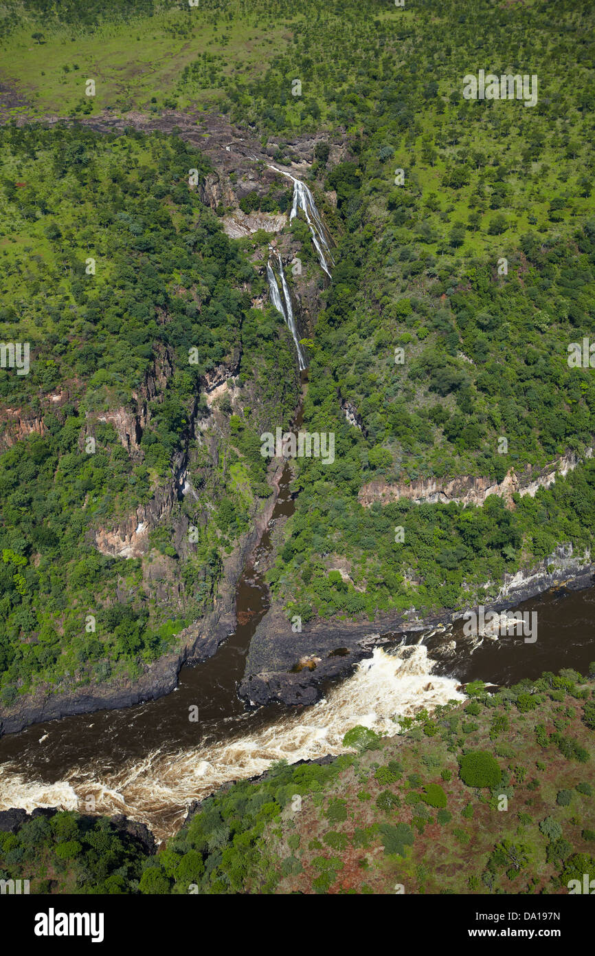 Waterfall flowing into Zambezi River in Batoka Gorge below Victoria Falls, Zimbabwe / Zambia Border, Southern Africa - aerial Stock Photo