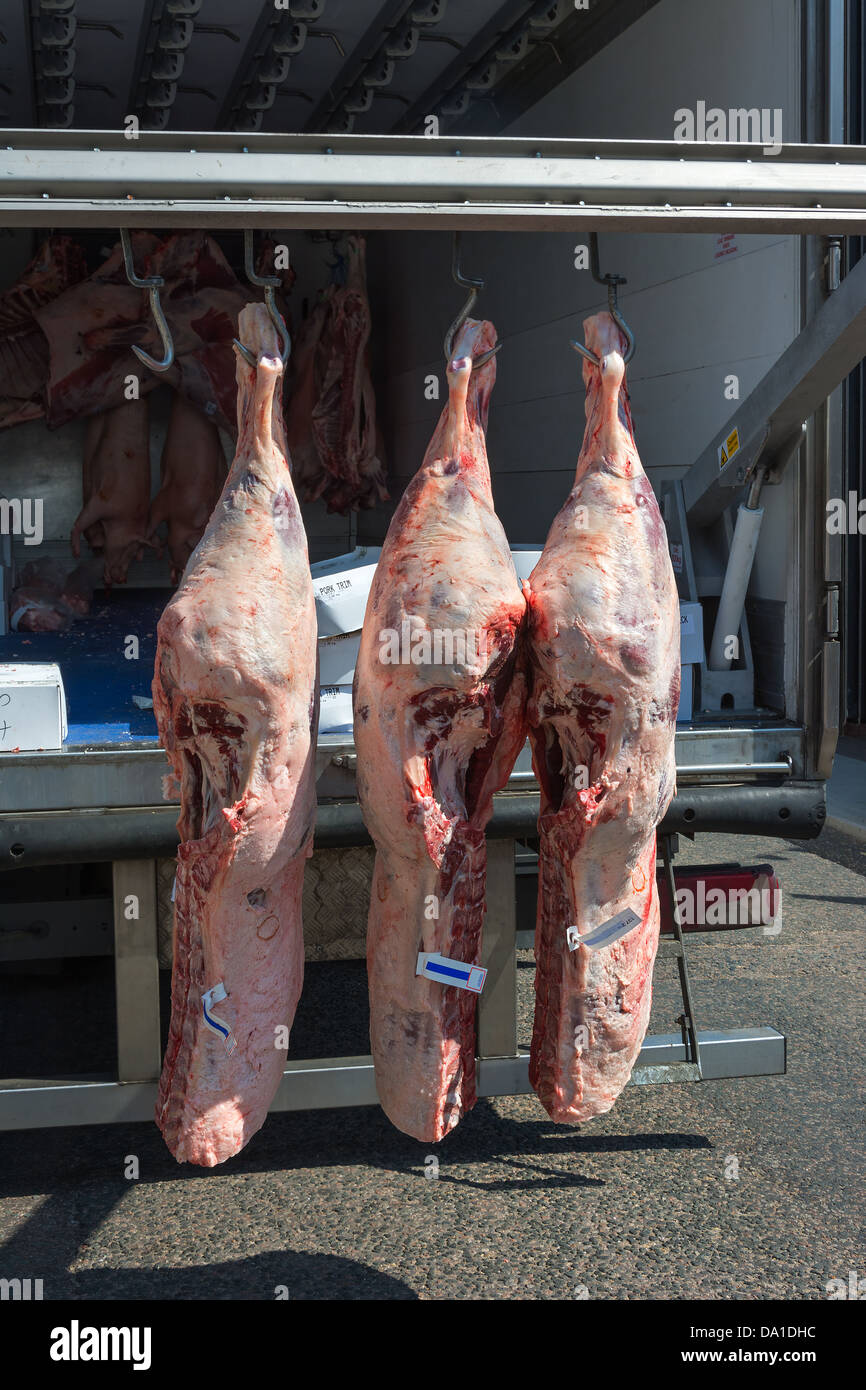 Meat being delivered to a butcher's shop hanging from the delivery van. Stock Photo