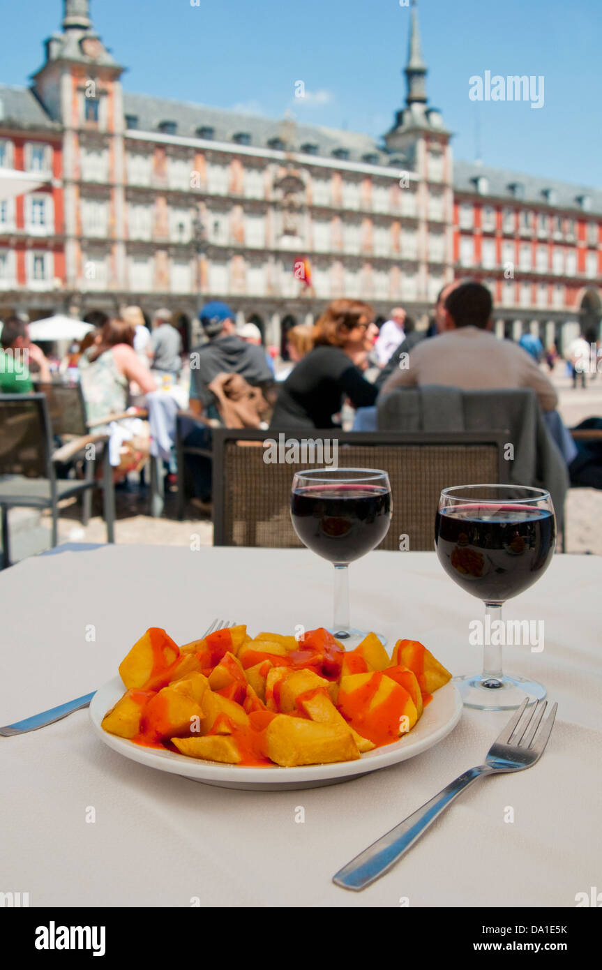 Spanish appetizer: Patatas bravas serving with two glasses of red wine in a terrace. Main Square, Madrid, Spain. Stock Photo