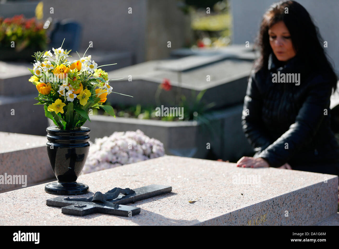 Woman praying at a grave in a cemetery. Stock Photo