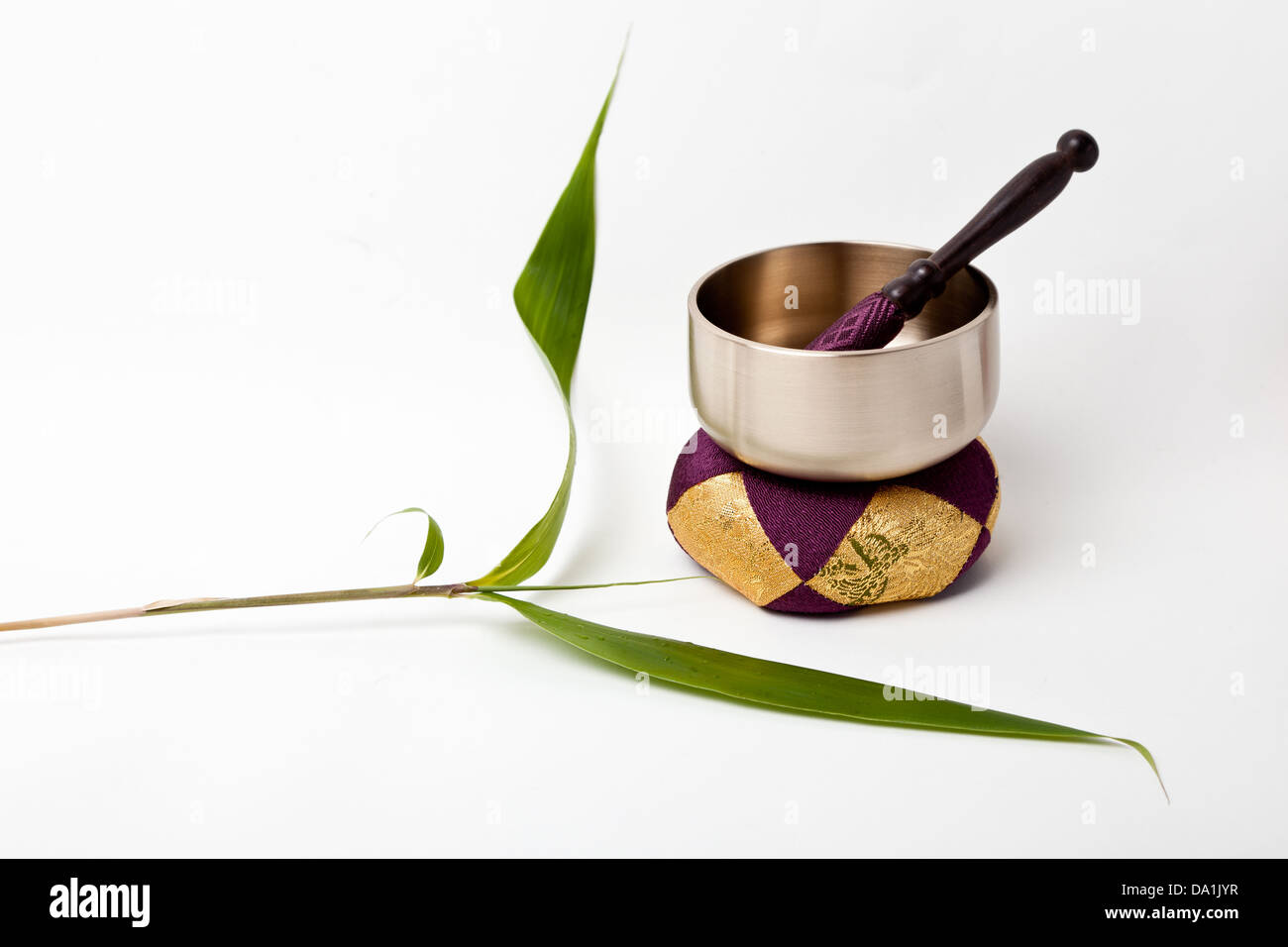 An isolated image of a Japanese Buddhist rin gong standing on a cushion with the stiker inside the gong and a piece of Sasa bamboo. With space for copy. Stock Photo