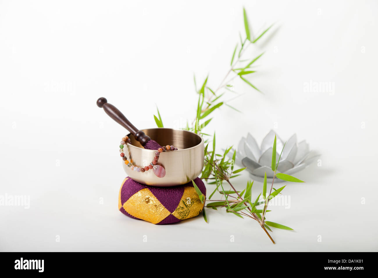 A Buddhist Rin gong on a cushion with the gong striker and prayer beads inside with a sprig of bamboo and a lotus flower shaped candle holder. Isolated on white. Stock Photo