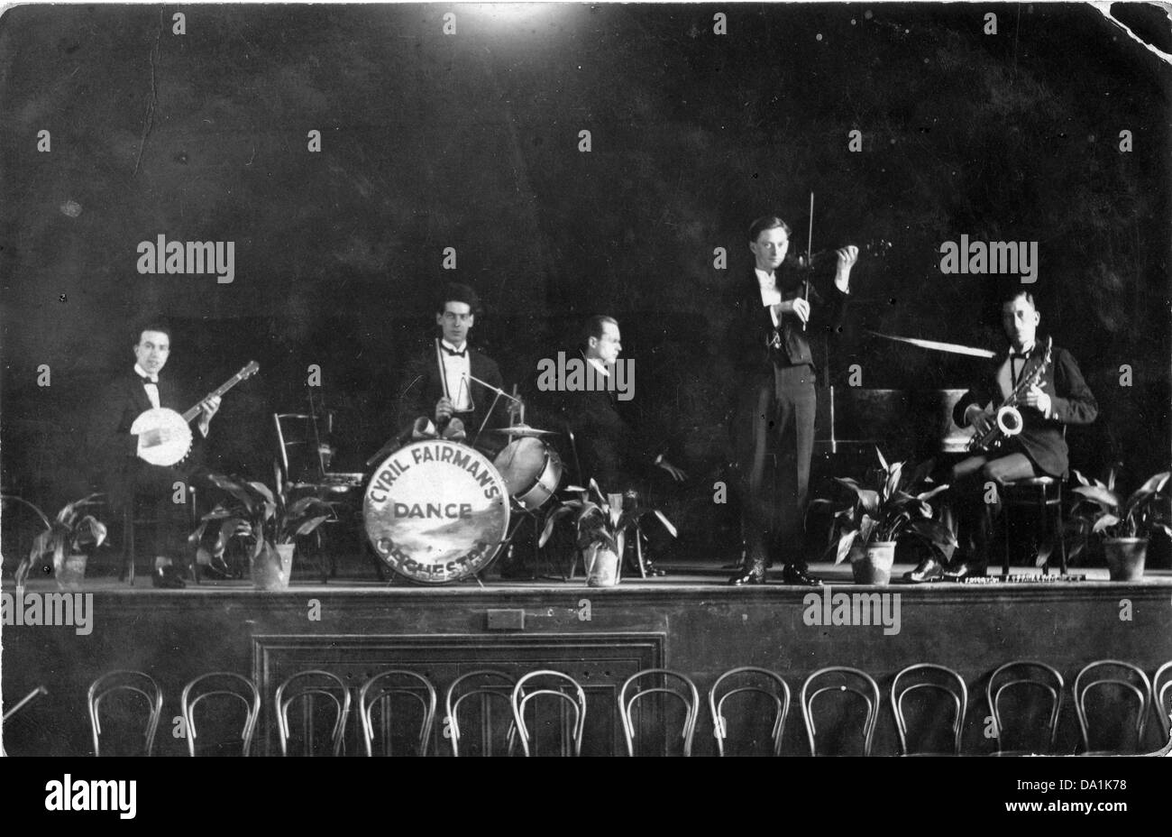 Black and white photograph of the Cyril Fairman dance band posing with instruments on a stage with a row of wooden chairs in front, circa 1920. Stock Photo