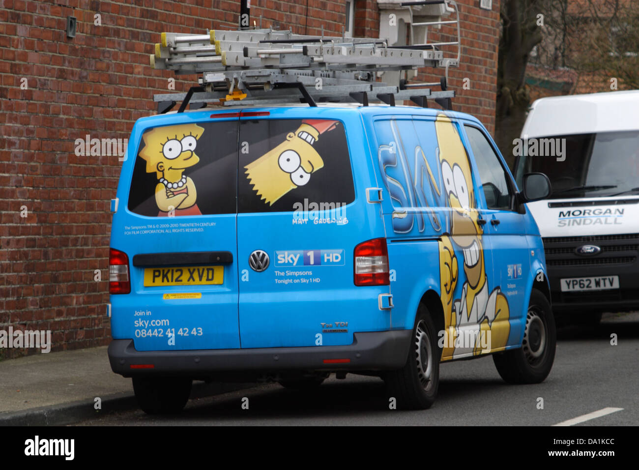 Sky Van, illustrated with Simpsons characters, bart, homer, lisa, ladders on top, white van in front. Parked outside a house. Stock Photo