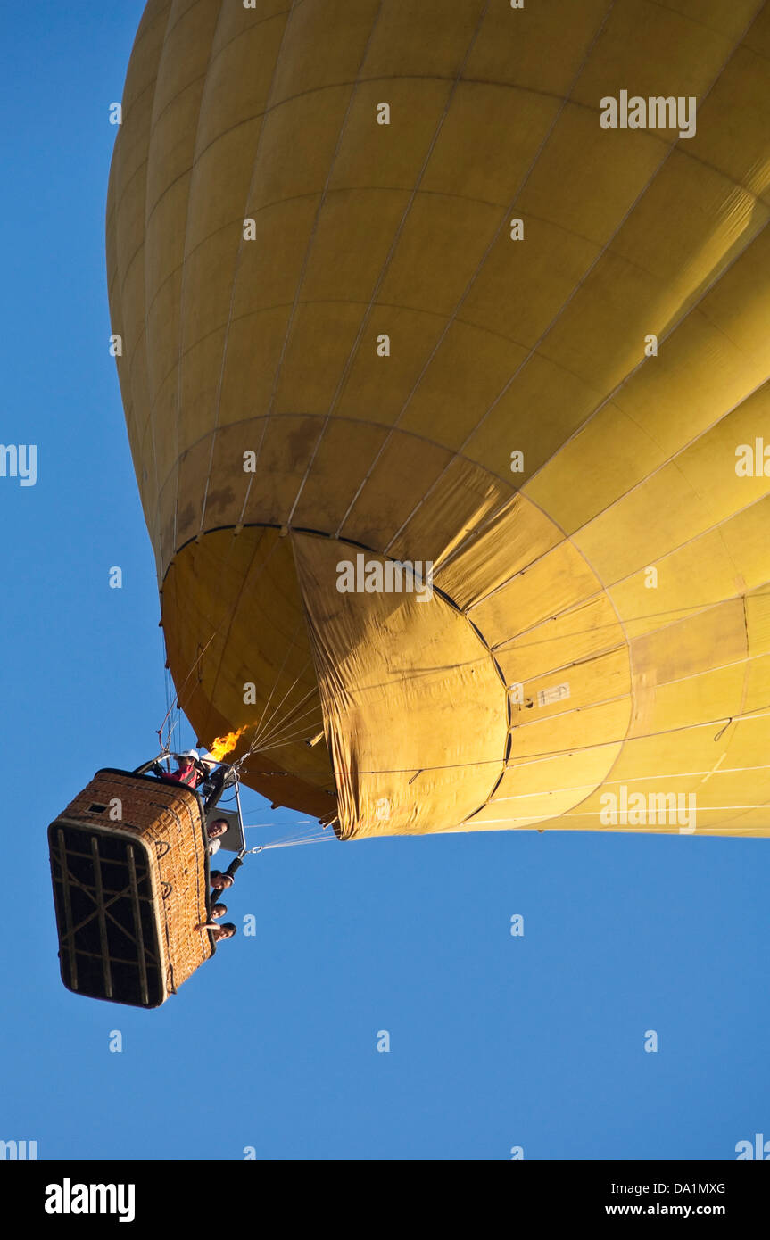 Vertical view of a yellow hot air balloon in flight with passengers against a blue sky. Stock Photo