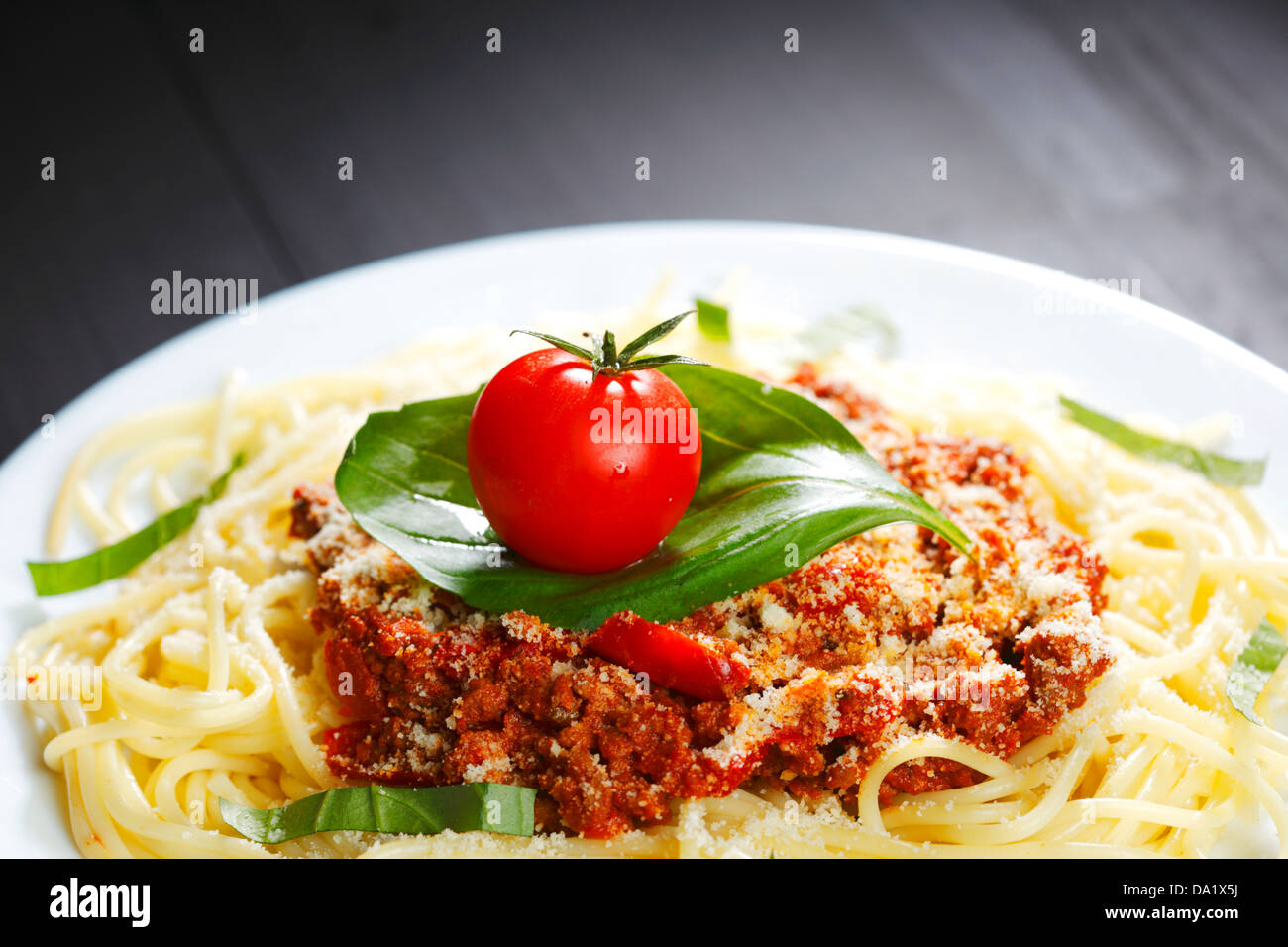 Spaghetti bolognese with fresh basil and tomato in white plate on back