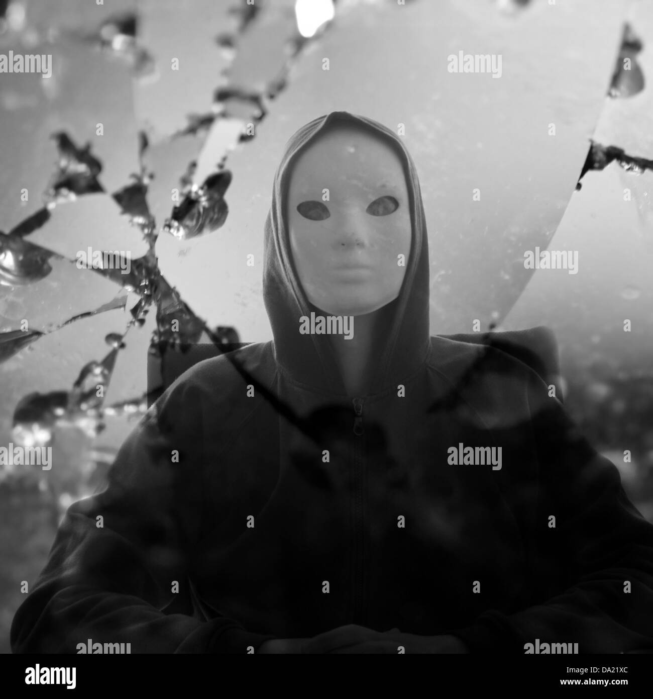 Masked figure reflected through broken glass mirror. Black and white. Stock Photo