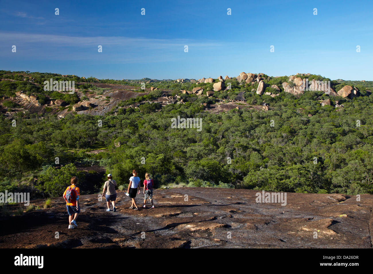 Tourists hiking above Big Cave Camp (in distance) blending in to the granite outcrops of the Matopos Hills, Zimbabwe, Africa Stock Photo