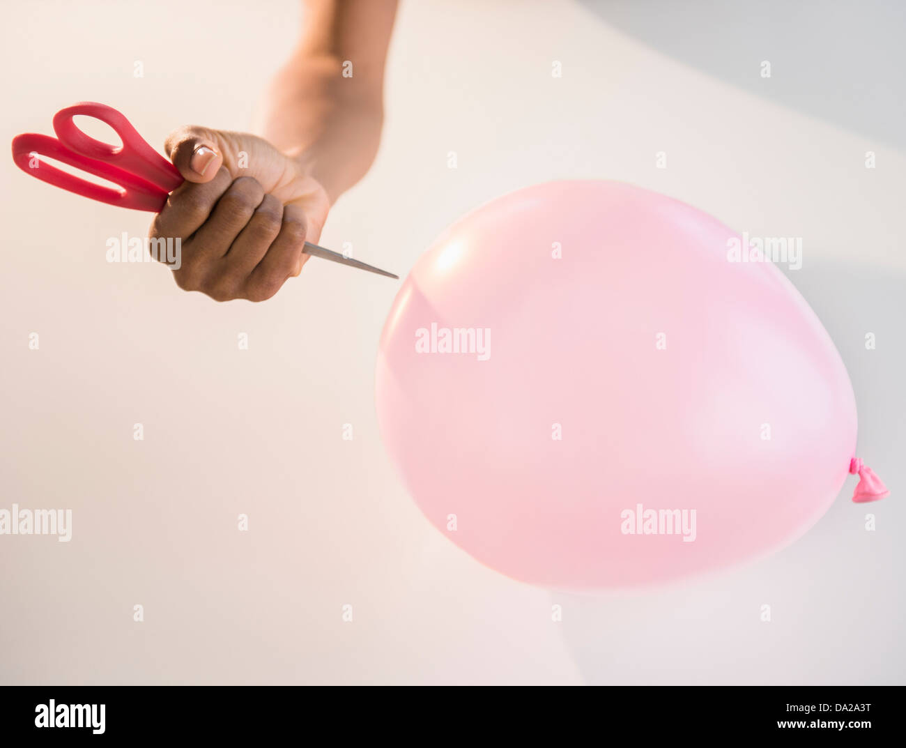 Close up of woman's hand popping balloon with scissors Stock Photo