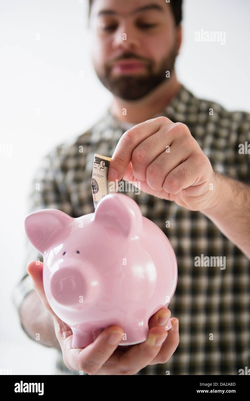 Portrait of man holding piggy ban and putting money inside Stock Photo ...