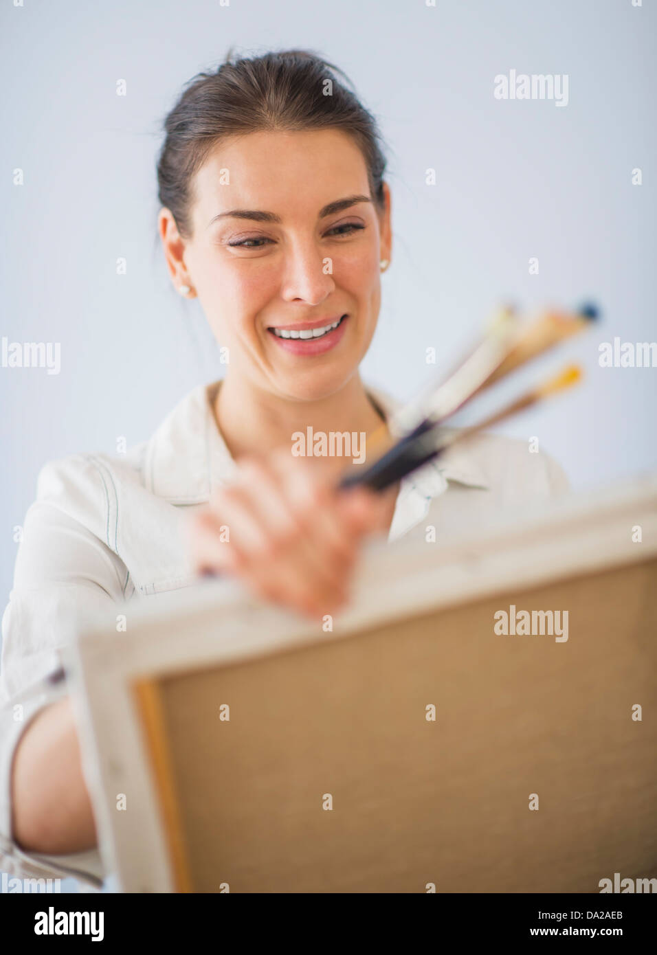 Studio Shot of woman holding paintbrushes and artist's canvas Stock Photo