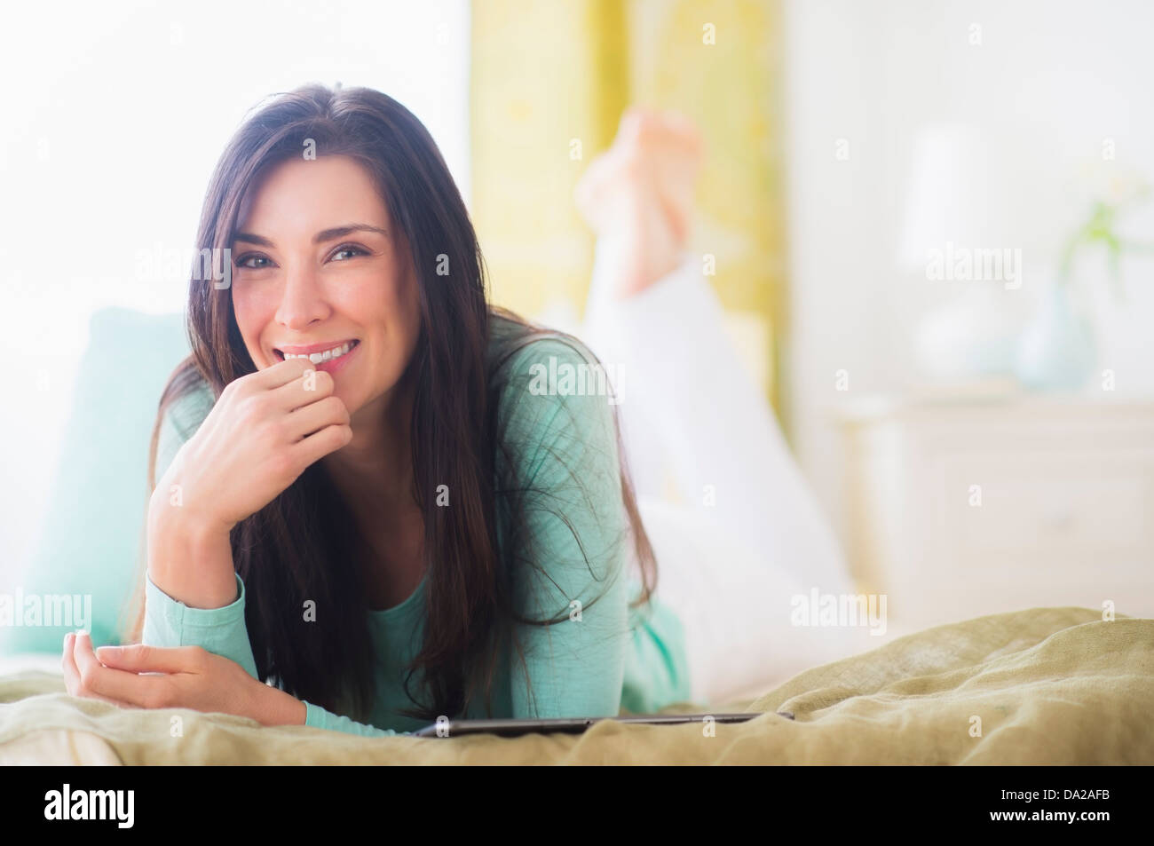 Portrait of woman lying down on bed with hand on chin Stock Photo