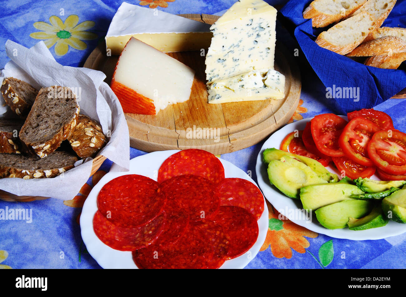French Brie, Spanish Manchego and French Bleu D’Auvergne cheeses with salami, avocado and tomato and bread. Stock Photo