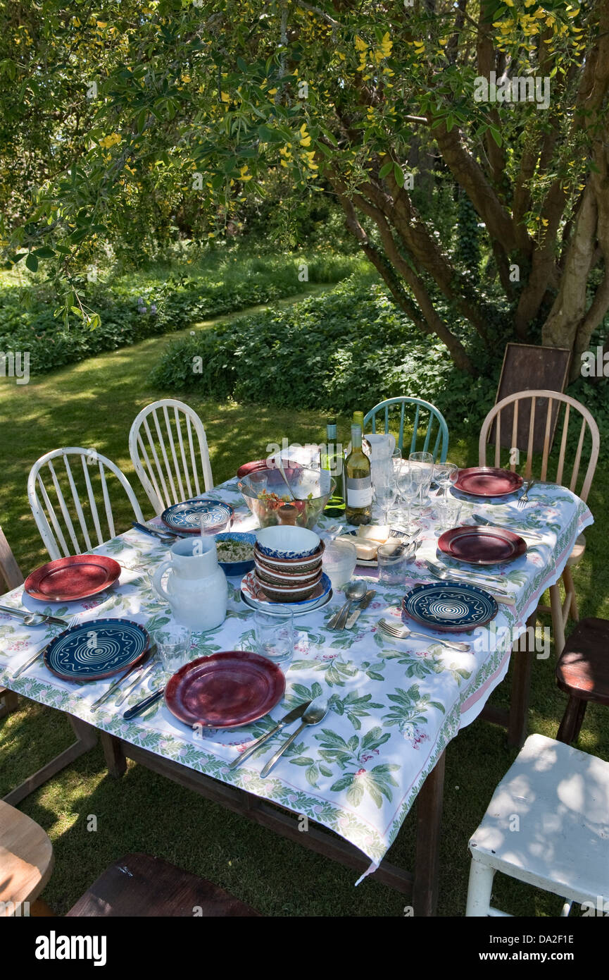 A table laid for lunch in the garden in the shade of a laburnum tree, on a hot summer day, UK Stock Photo
