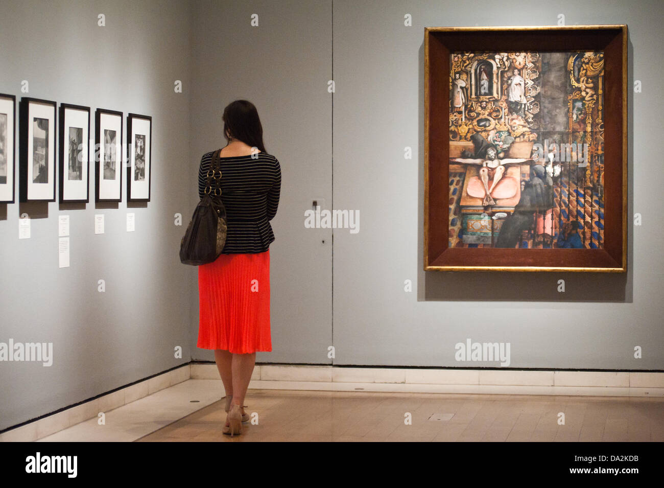 London, UK - 2 July 2013: a visitor stands next to a work by entitled at the exhibition 'Mexico: A Revolution  London, UK - 2 July 2013: A woman walks next to a work by Edward Burra entitled 'Mexican Church, 1938' at the exhibition 'Mexico: A Revolution in Art, 1910–1940' which opens on the 6th of July. The show features over 120 paintings and photographs and examines the intense period of artistic creativity that took place in Mexico at the beginning of the 20th century.   in Art, 1910–1940' which opens at the Royal Academy of Arts on the 6th of July.  Stock Photo