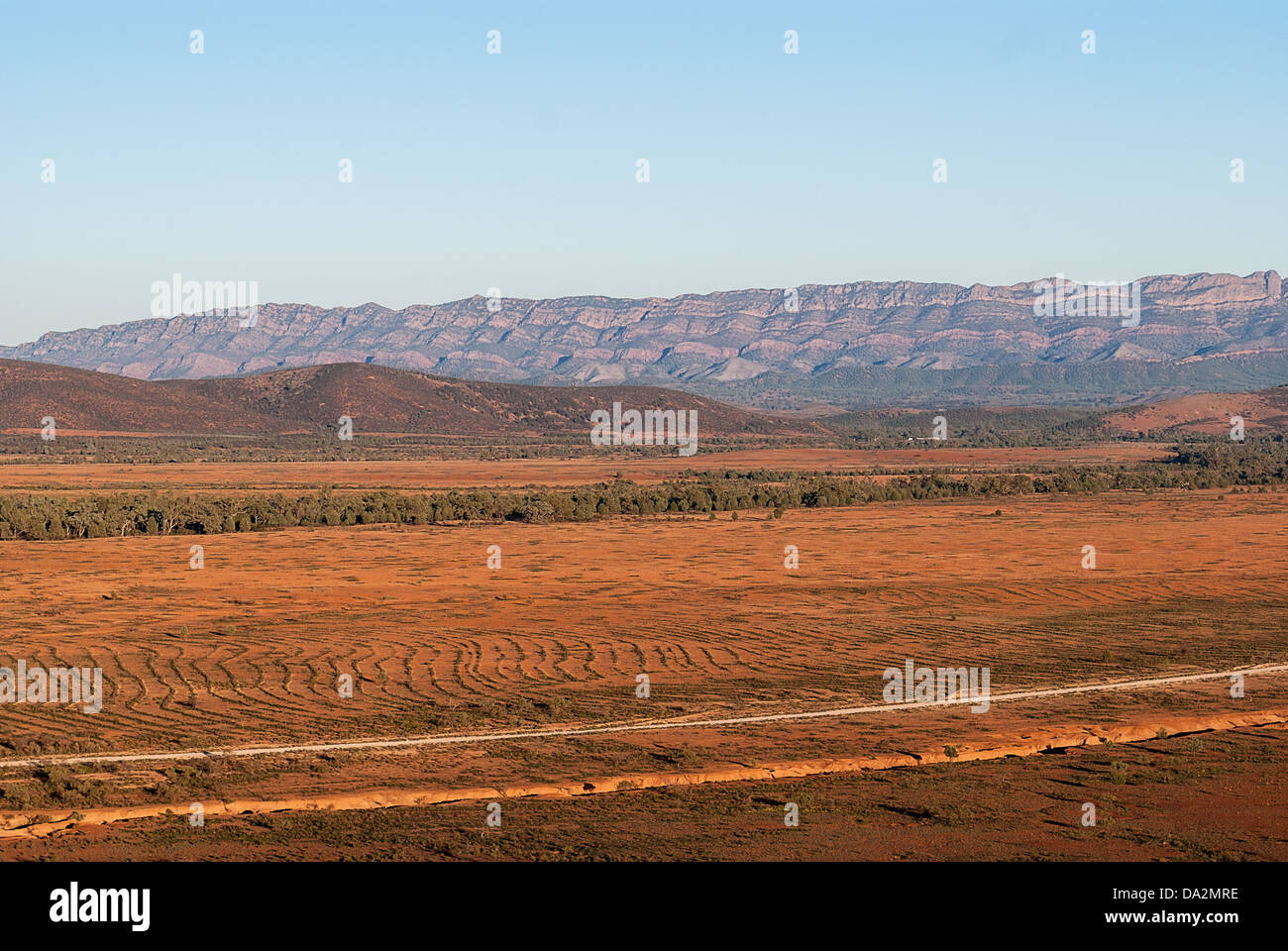 A dusty outback road winds through bushland towards distant ranges lit ...