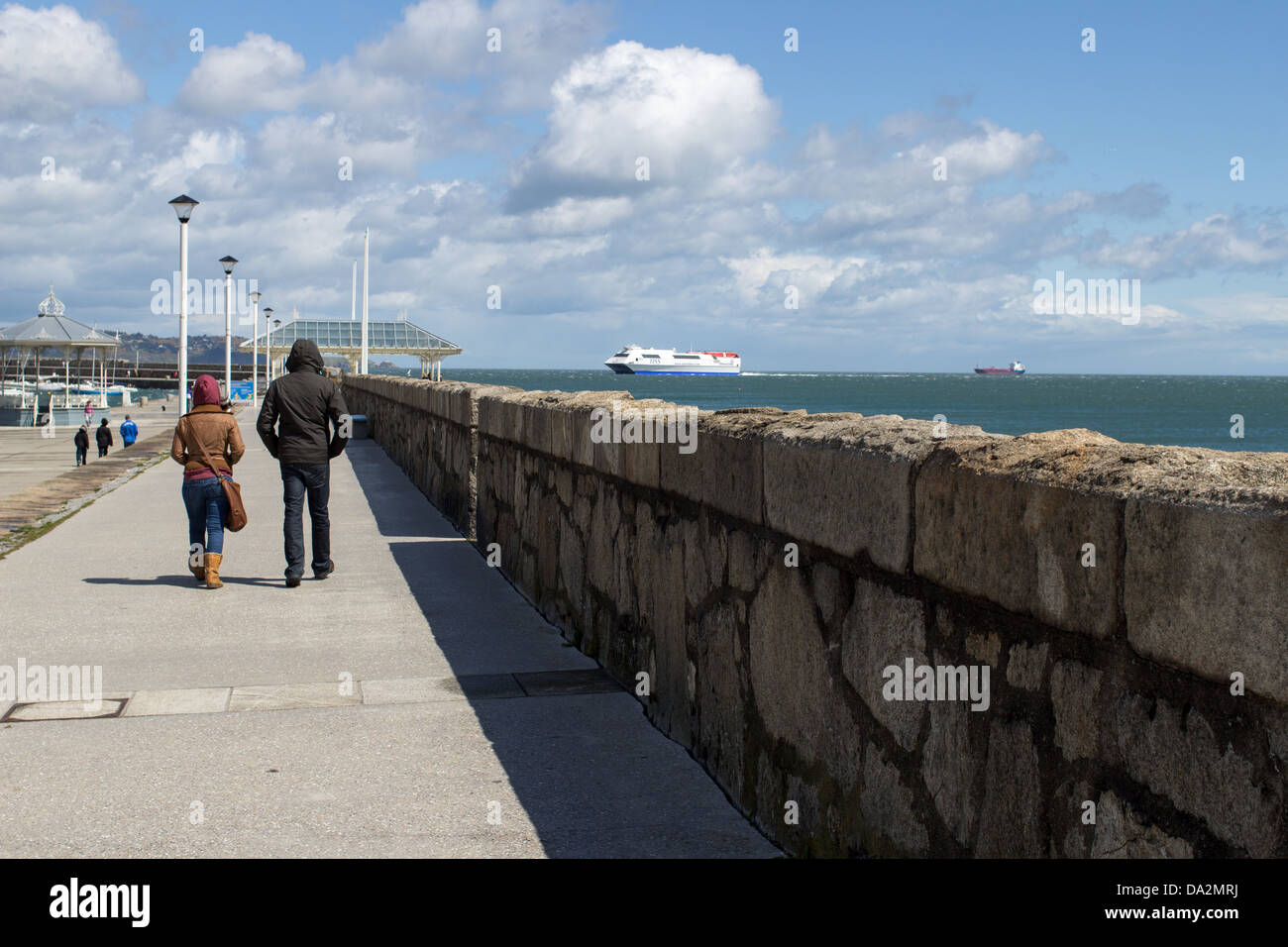 People walking on a promenade with a ferry in the background. Stock Photo