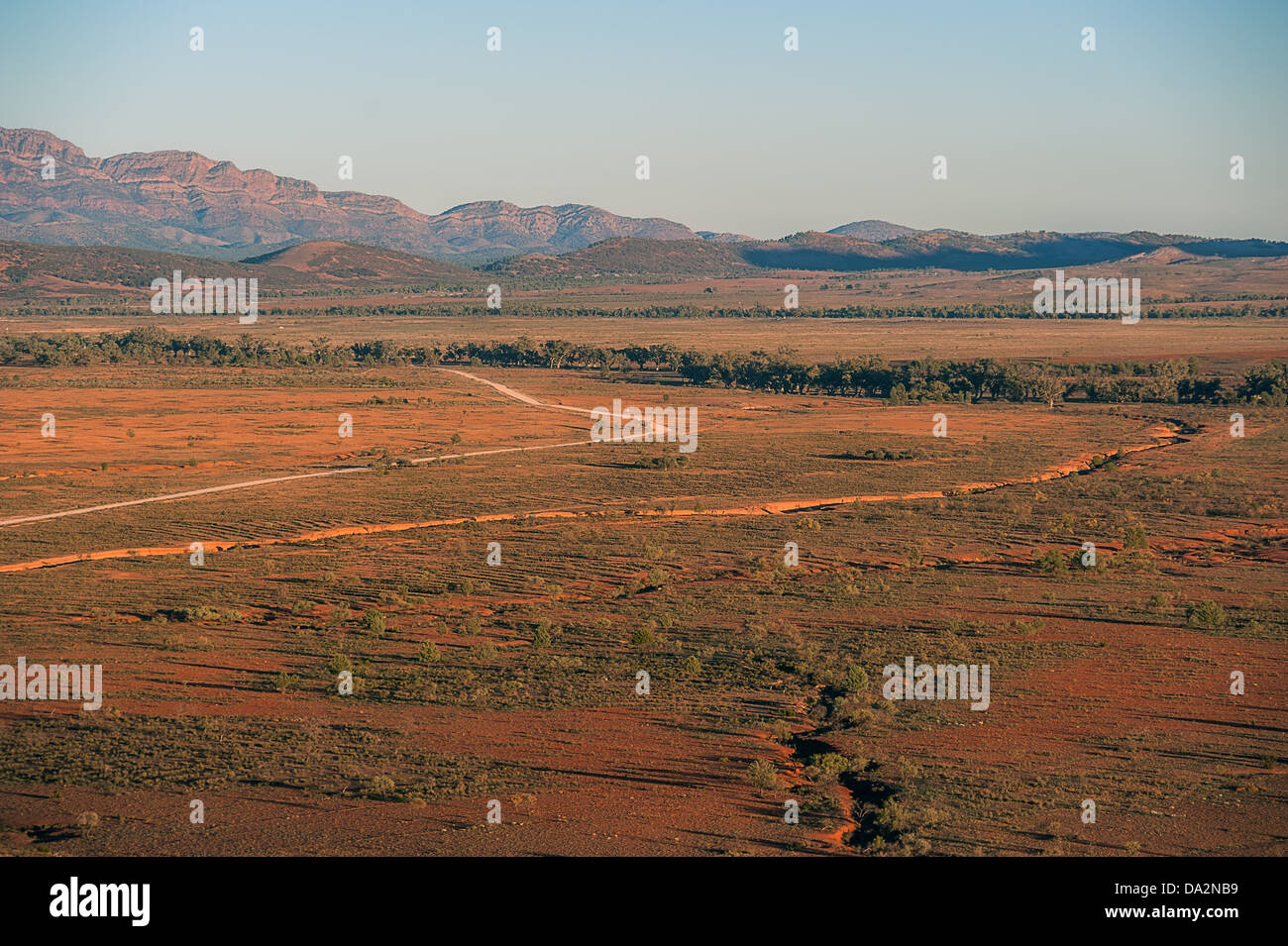 A dusty outback road winds through bushland towards distant ranges lit ...