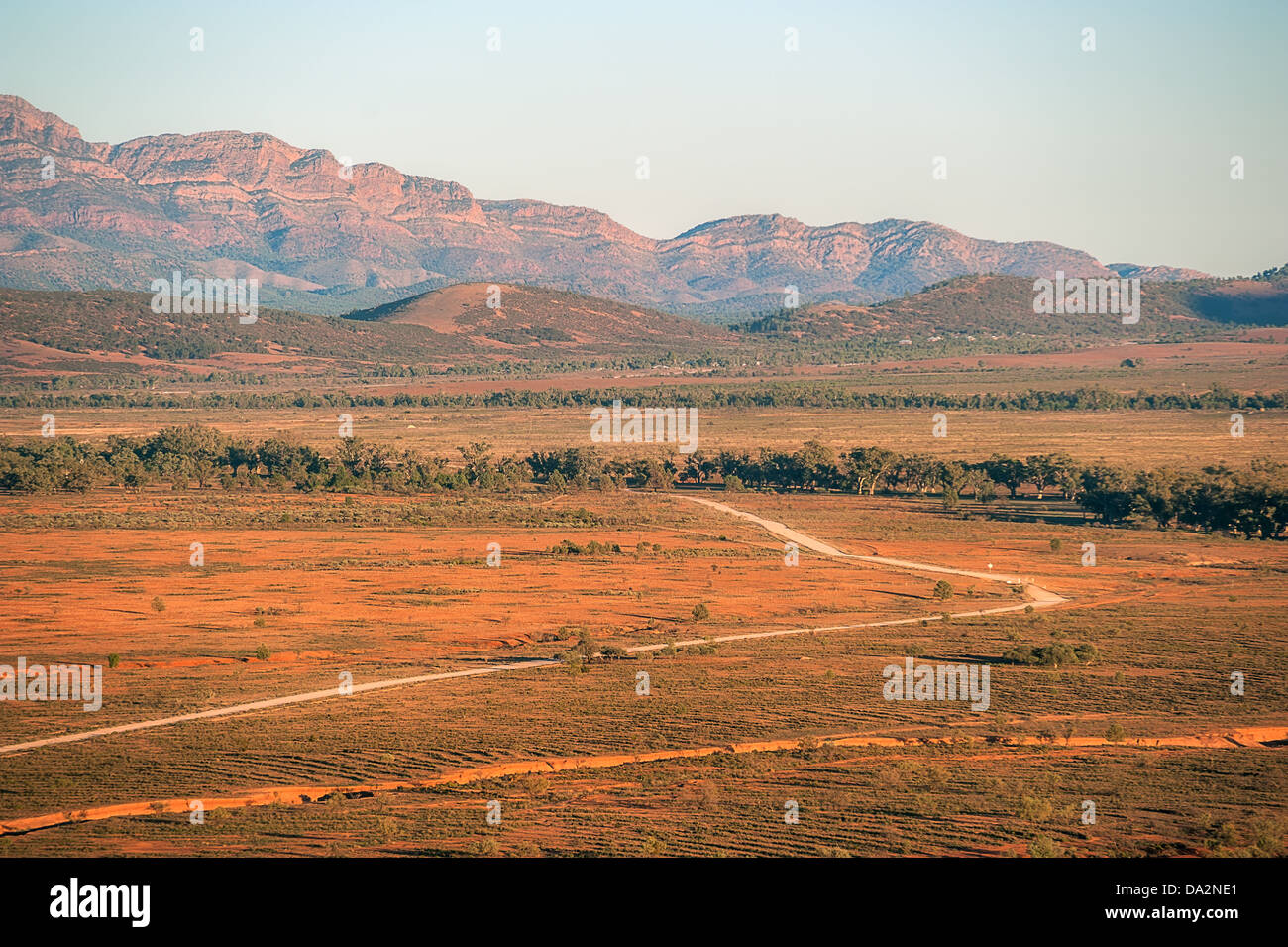 A dusty outback road winds through bushland towards distant ranges lit ...