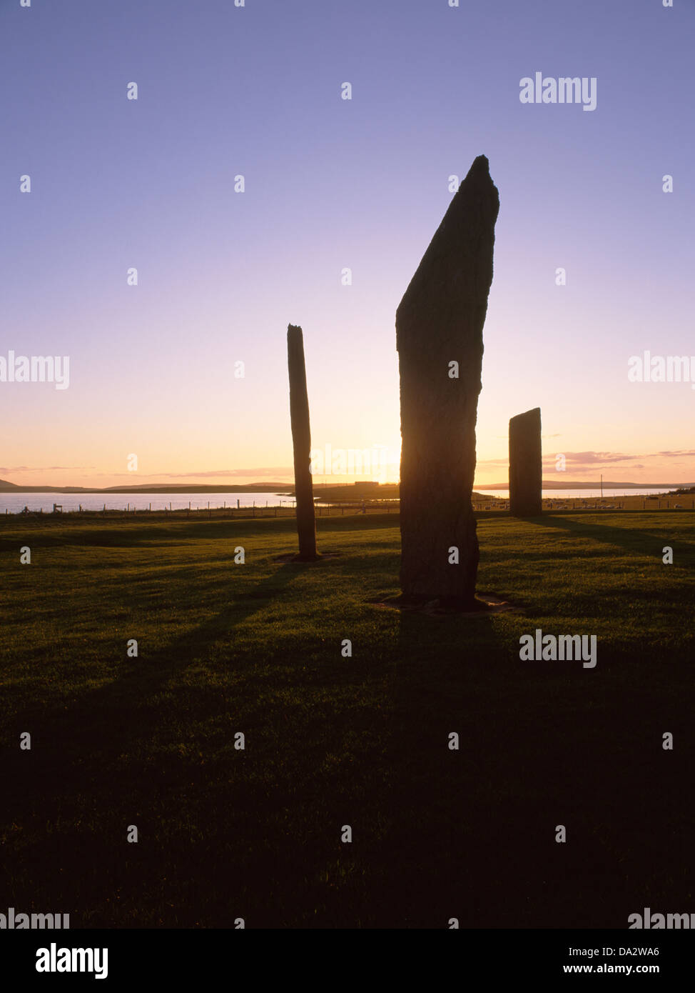 Looking NW at the Stones of Stenness stone circle, Mainland, Orkney, backlit by the setting sun. Ness of Brodgar, Lochs Stenness & Harray to rear. Stock Photo