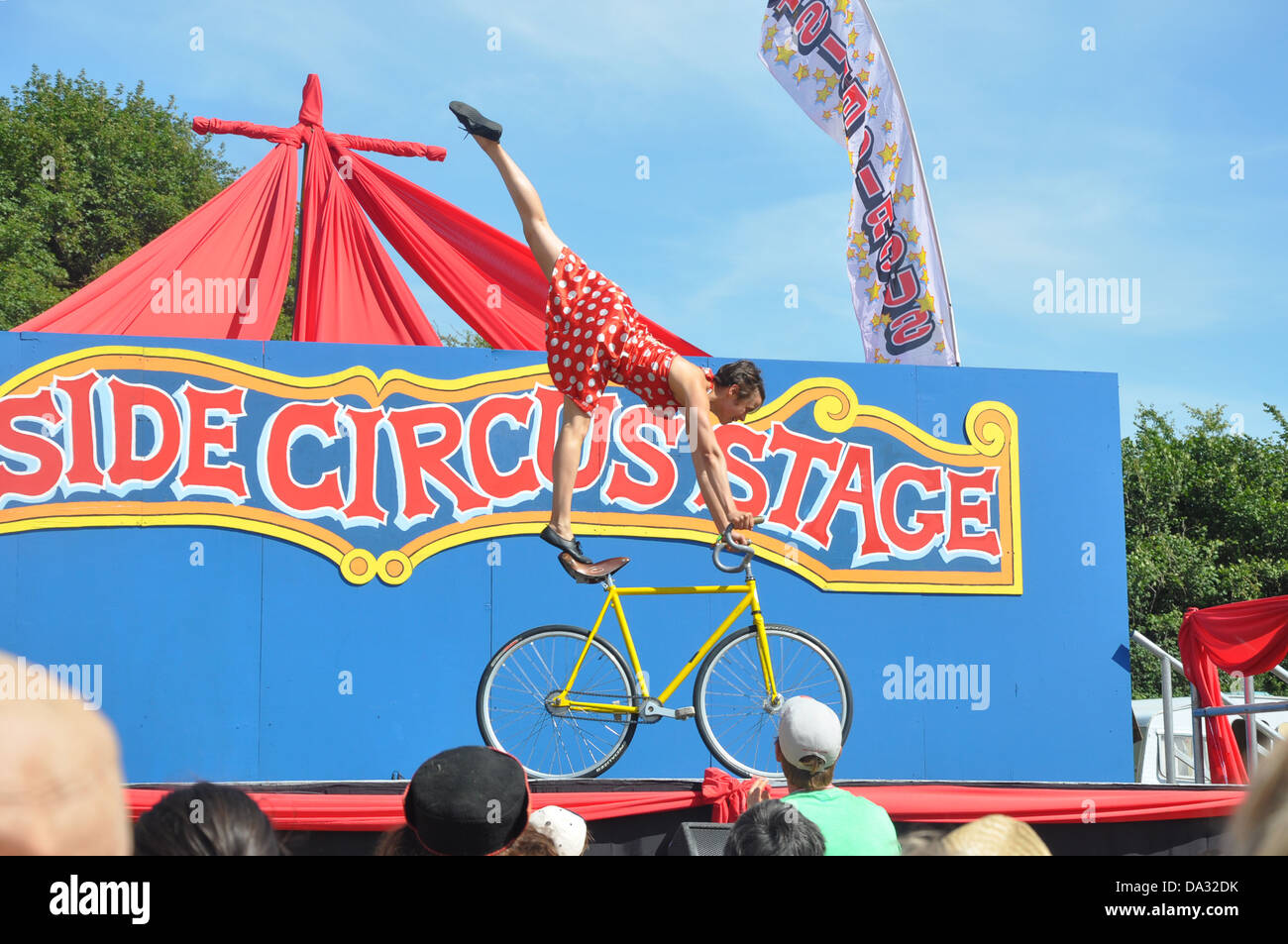 A circus performer does a routine with her bicycle on the Outside Circus Stage at Glastonbury Festival 2013 Stock Photo
