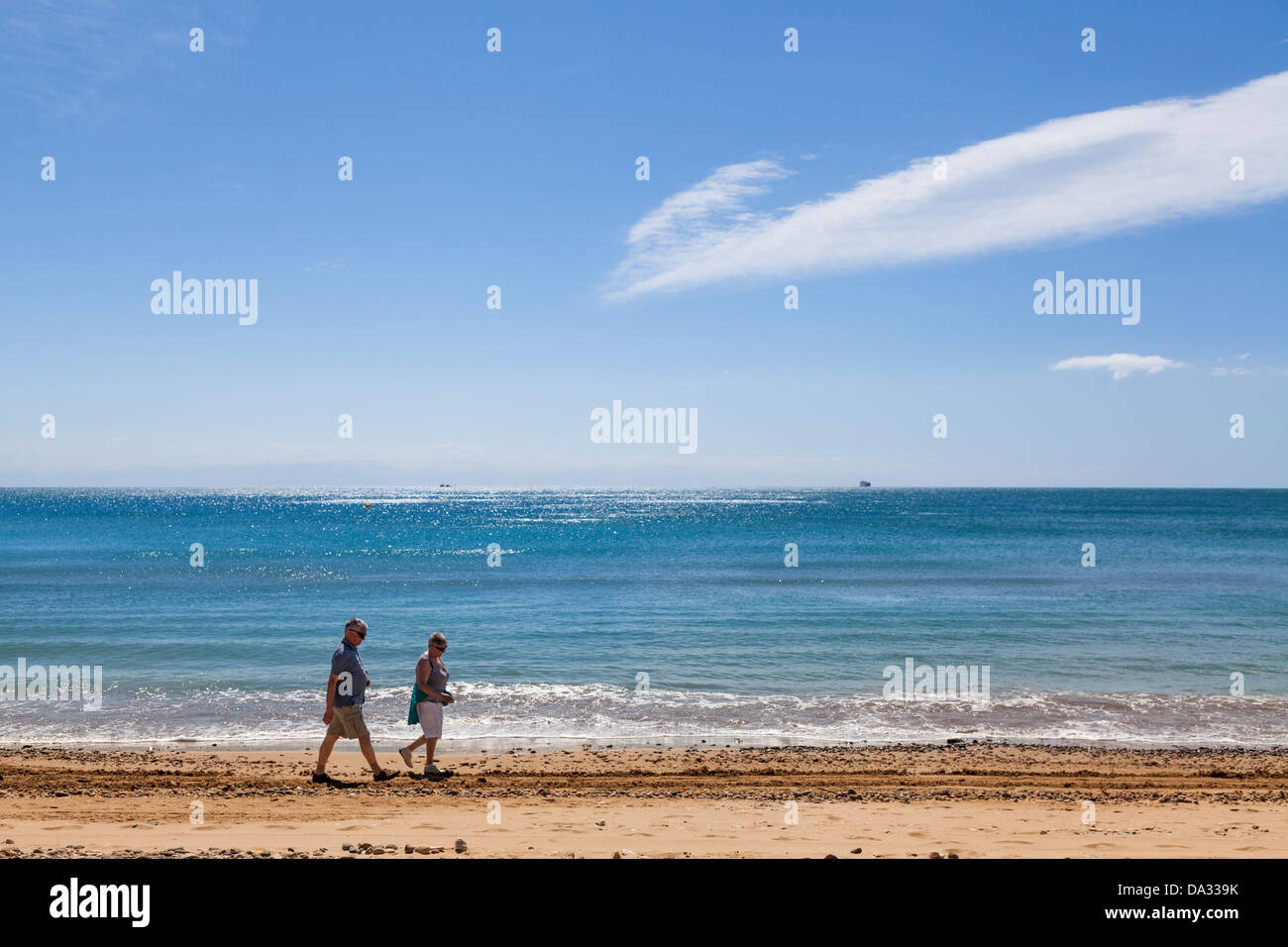 Middle aged couple walking along the waters edge on the beach. Stock Photo