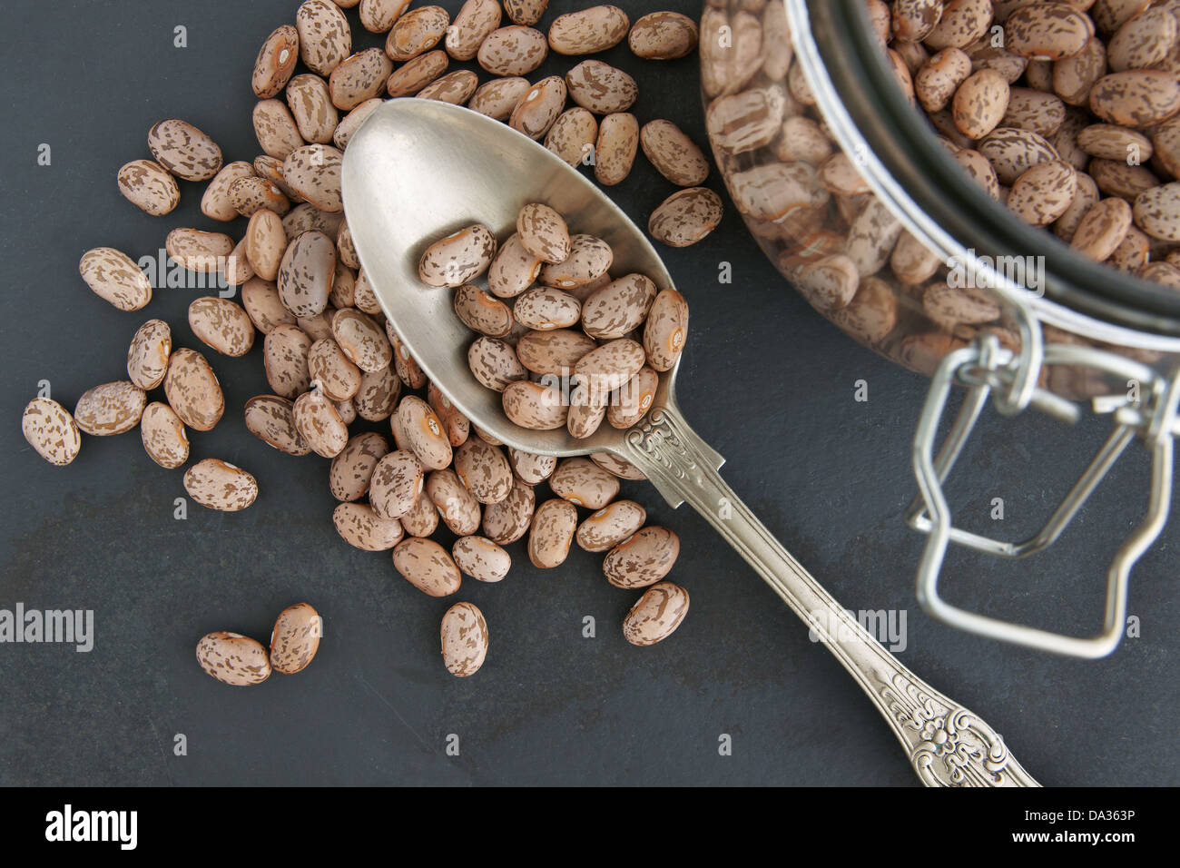 Pinto Beans with an antique silver spoon on a slate background and defocussed storage jar Stock Photo
