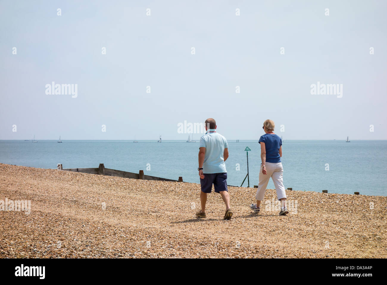 Man and Woman Couple Walking Along Beach on Hayling Island Hampshire Stock Photo