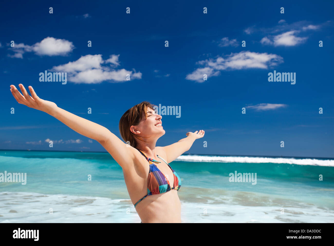 Beautiful young woman with arms open in a tropical beach enjoying the summer Stock Photo