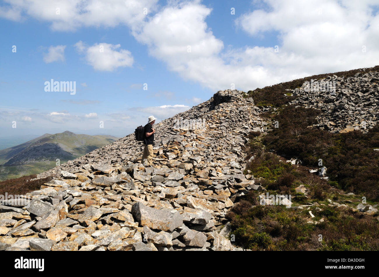 Man walker standing on the thick stone outer wall of Tre'r Ceiri iron Age Hill Fort Yr Efil The Rivals Llyn Peninsula Wales UK Stock Photo