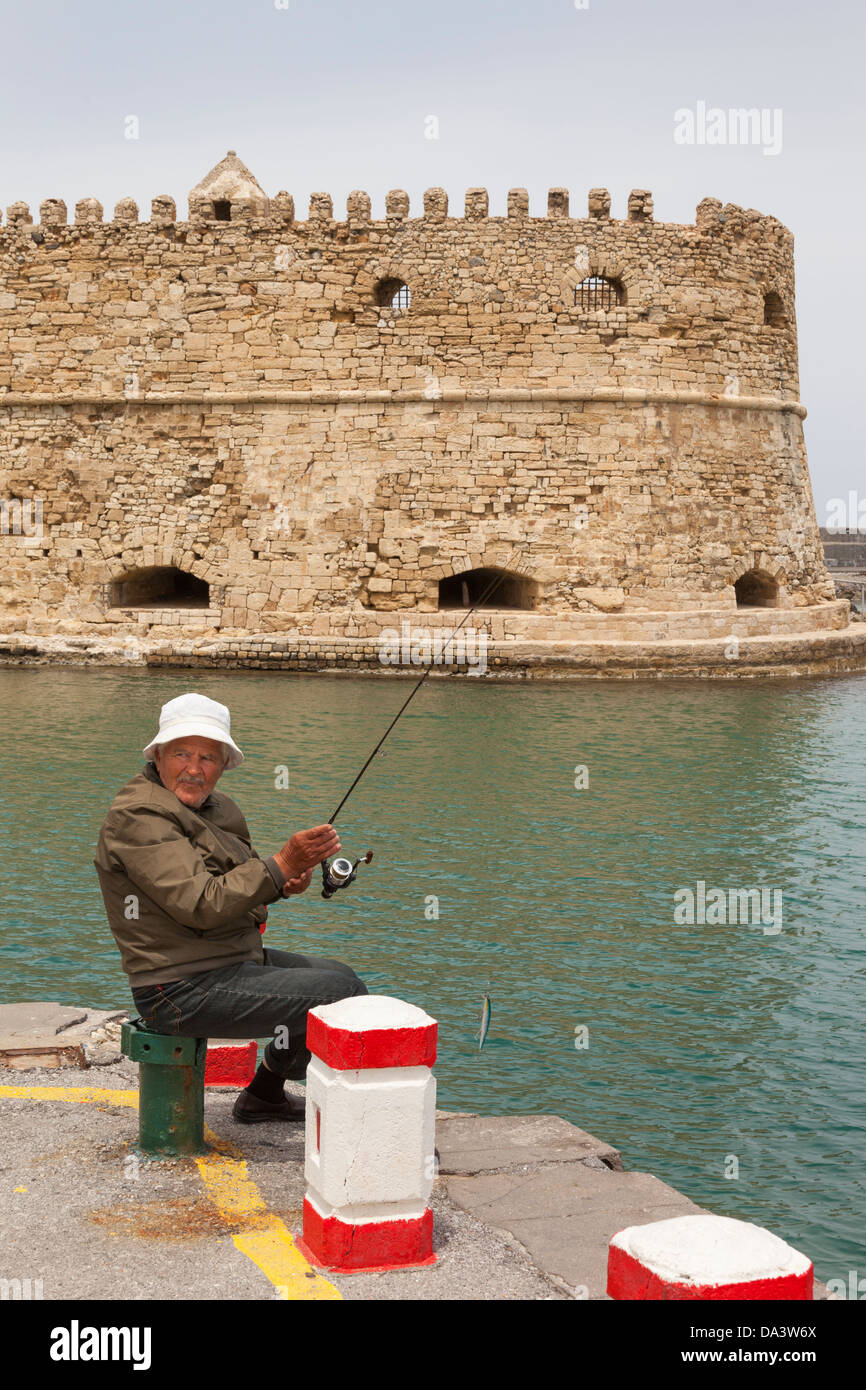 Man fishing beside Koules Fort in the Venetian Harbour, Heraklion, Crete, Greece Stock Photo