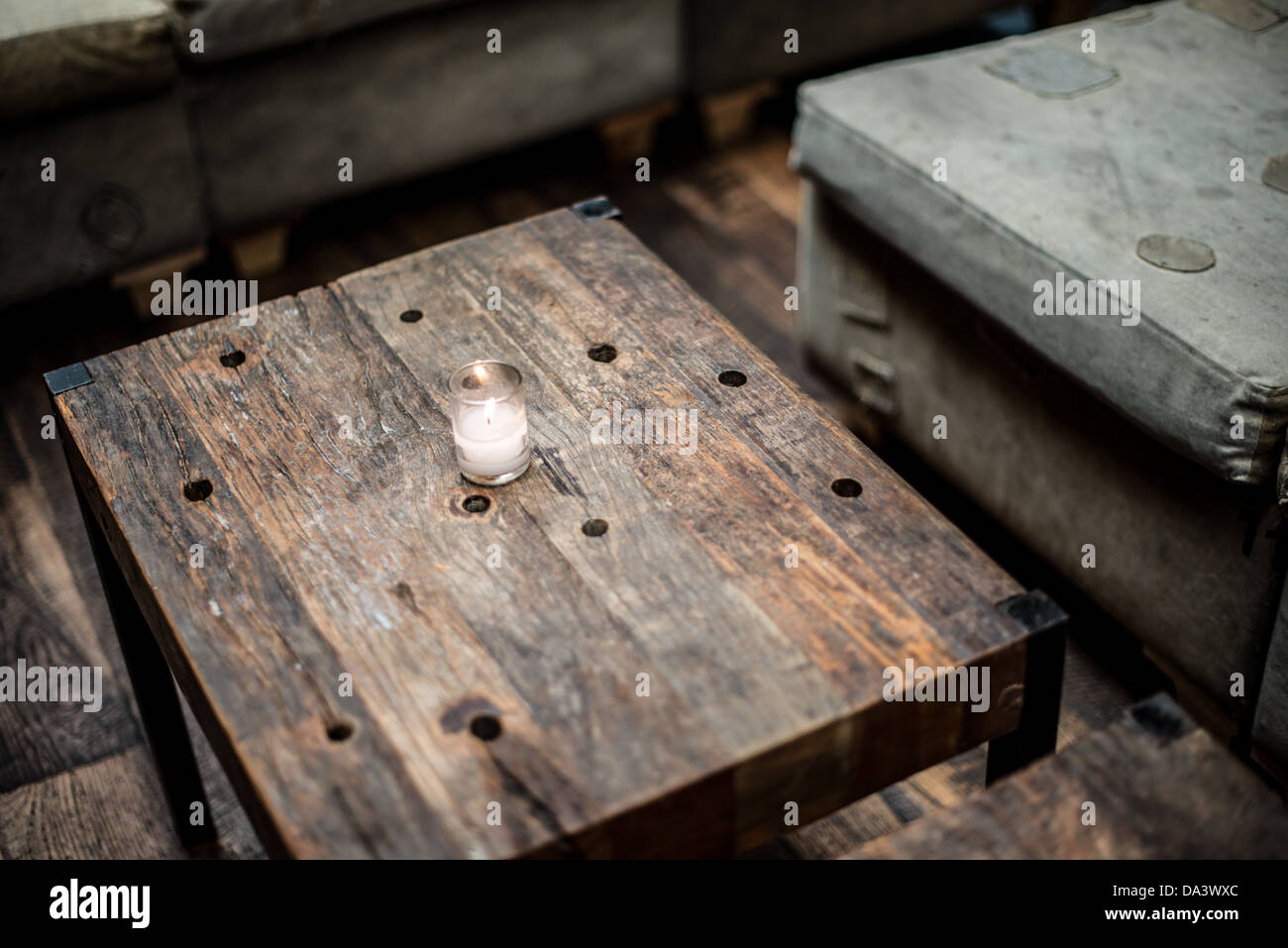 A small votive candle ssits on a rustic wooden table in a restaurant bar. Stock Photo