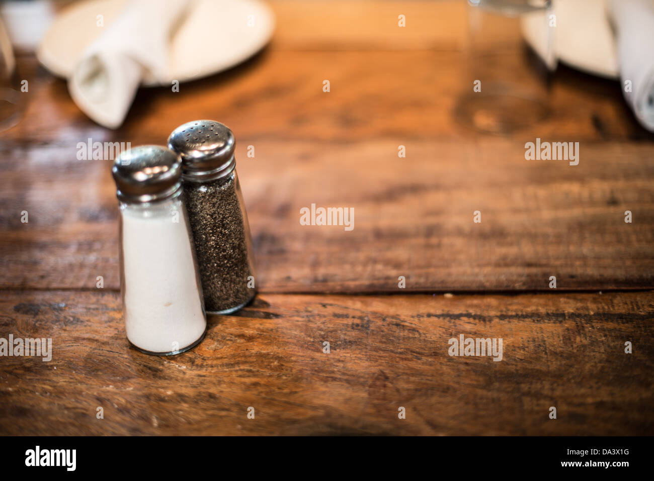 Ground salt and pepper shakers on a polished wood surface with light from a  window illuminating the table; rustic dining table with glass shakers Stock  Photo - Alamy