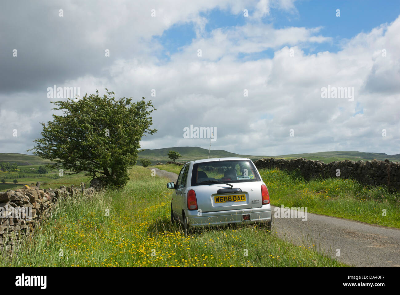 Small car parked on grass verge, next to narrow country lane, North Stainmore, Cumbria, England UK Stock Photo