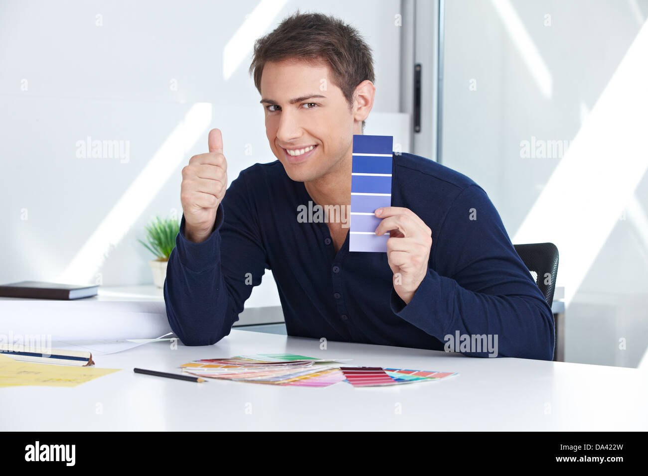 Designer with blue color samples at his desk in the office holding thumbs up Stock Photo